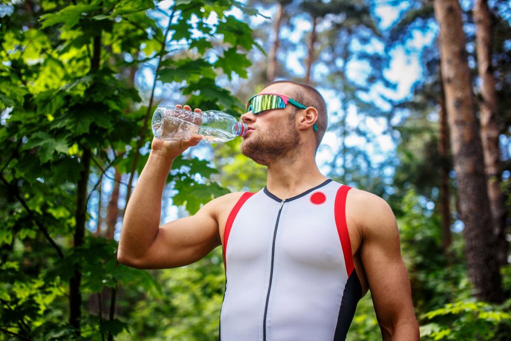 mezczyzna w sportowej i okulary przeciwsloneczne trzymajac butelke z woda