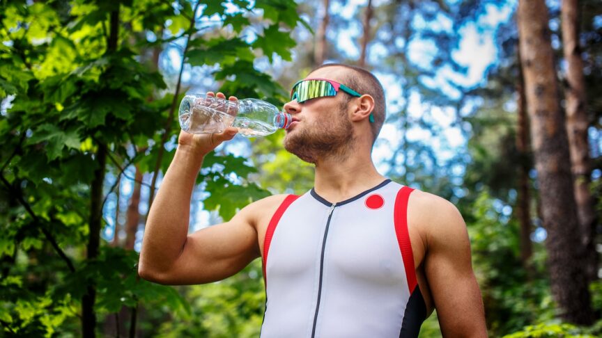 mezczyzna w sportowej i okulary przeciwsloneczne trzymajac butelke z woda