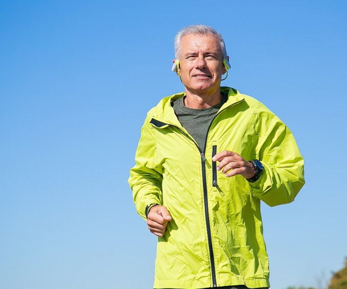 happy excited senior man wireless headphones jogging outside low angle blue clear sky front view copy space activity age concept